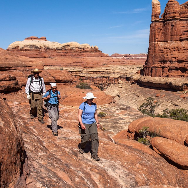 three people walk on red slickrock