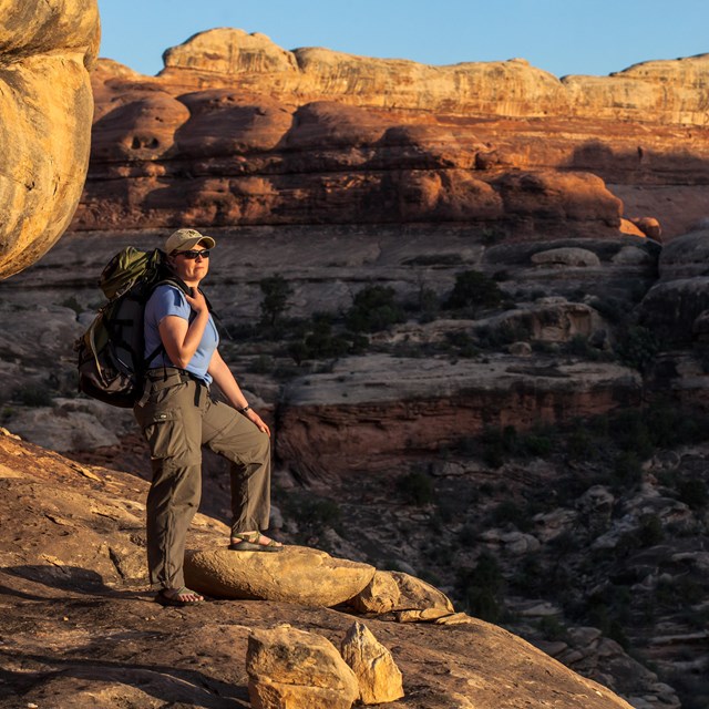 a backpacker stands on a ledge overlooking a canyon