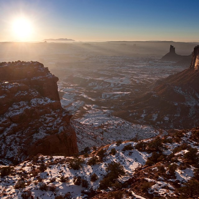 the sun sets behind tall cliff edges and pinnacles dusted with snow