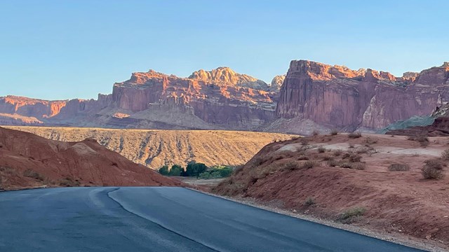 Hill top view next to a road with red sandstone cliffs in the distance.