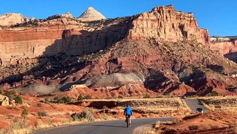 Cars and a bicyclist on a road which parallels sandstone cliffs