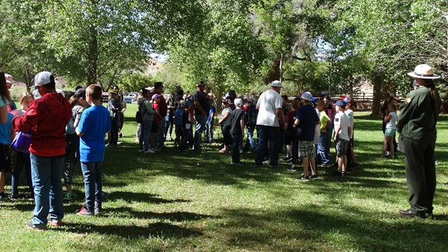 A ranger stands in a grassy open field surrounded by students
