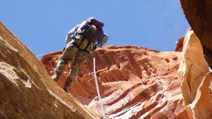Person rapelling down redrock cliff wall with blue sky above.