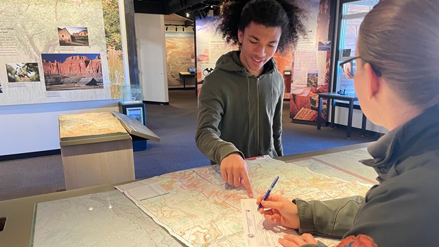 A person pointing at a map and a ranger filling out a form at a desk.