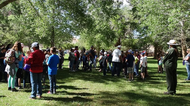 A ranger stands in a grassy open field surrounded by students