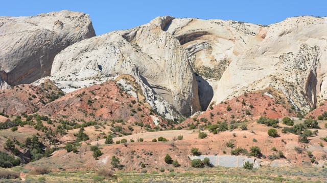 Blue sky, large white slopes, with red triangular shaped rocks below, green grass in the foreground