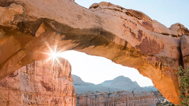 Sun shining from underneath a natural sandstone bridge, over 100 feet wide.