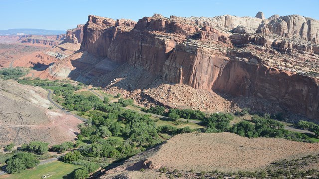 Green valley below colorful cliffs, with blue sky. 