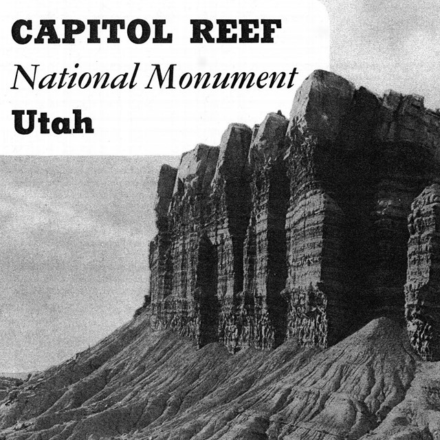 Black and white photo of a car and a small stone ranger station with giant cliffs above it. 