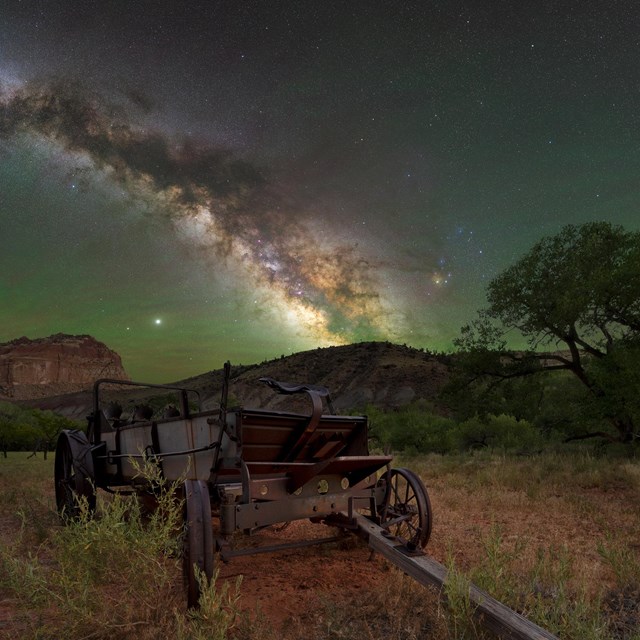 The Milky Way over an old wagon with cliffs and trees in the background