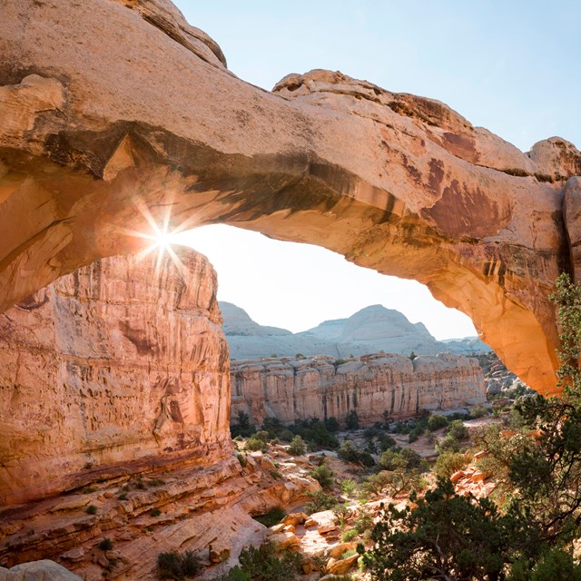 Sun shining from underneath a natural sandstone bridge, over 100 feet wide.