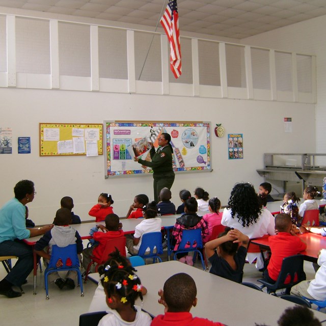 Head-Start students in a classroom, watching a ranger holding up park photos.