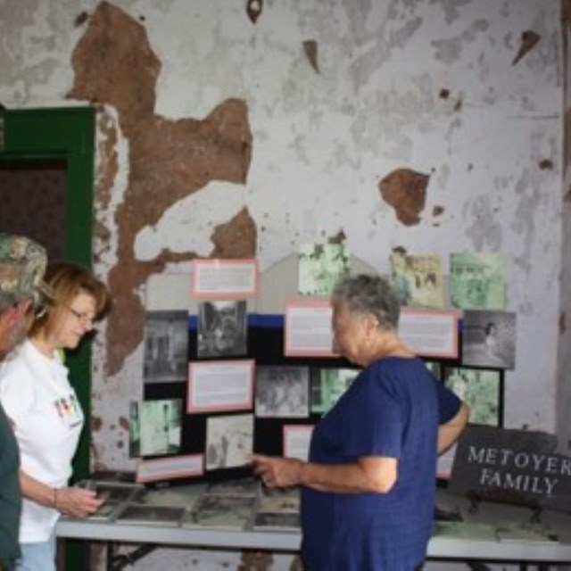 Mary stands before picture covered board, with two additional people listening and looking.