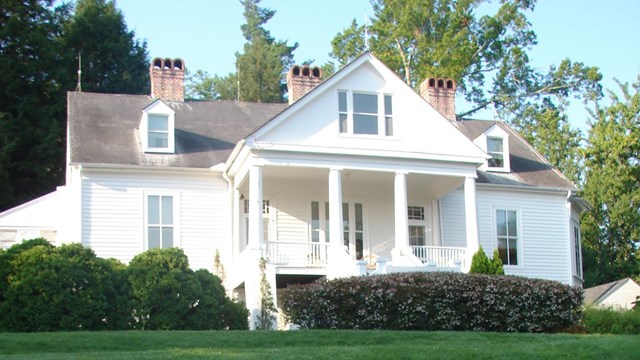 Image of white house on a hill with red flowers in the foreground
