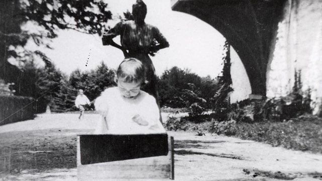 black and white image of a child playing in the foreground with a woman standing behind