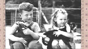 Black and white photo of two young children holding goats