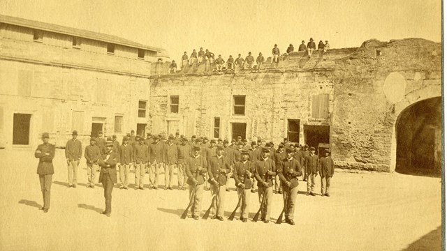 Picture shows many people in US Army Uniforms standing in the fort's courtyard.