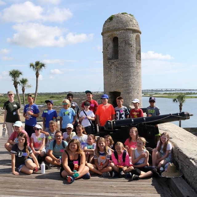 Field trip of students on gun deck near cannon and bell tower. 