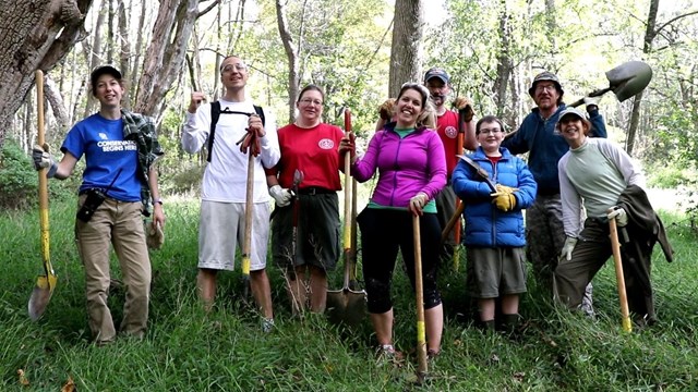 A group of volunteers holds shovels and loppers.