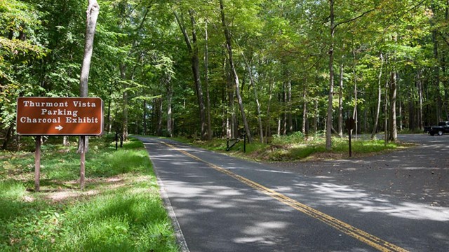 Image of Sign with Directional Arrow Pointing to Parking Area Alongside a Road