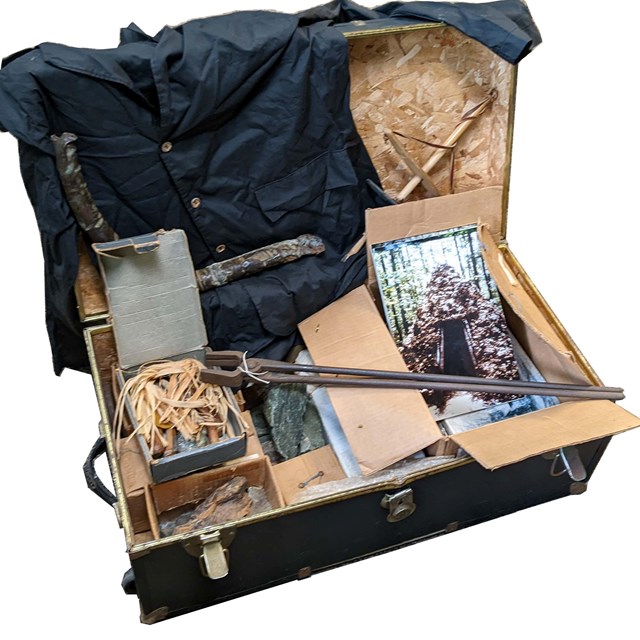 An open trunk with historical artifacts including a shirt and iron tongs