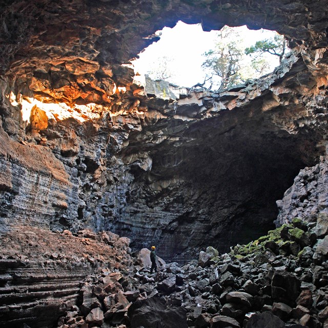 a person standing in a large lava tube with collapse hole in the ceiling showing daylight