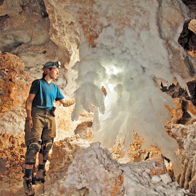 a caver stands next to a large white crystal formation 