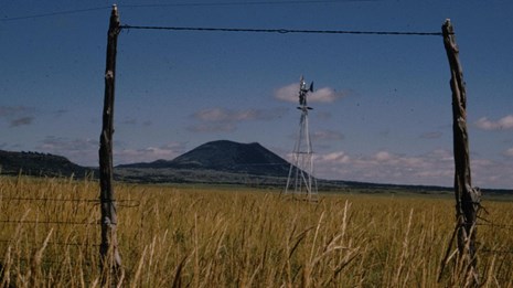 Capulin Volcano, in the distance, is framed by gate posts and a windmill from the plains.