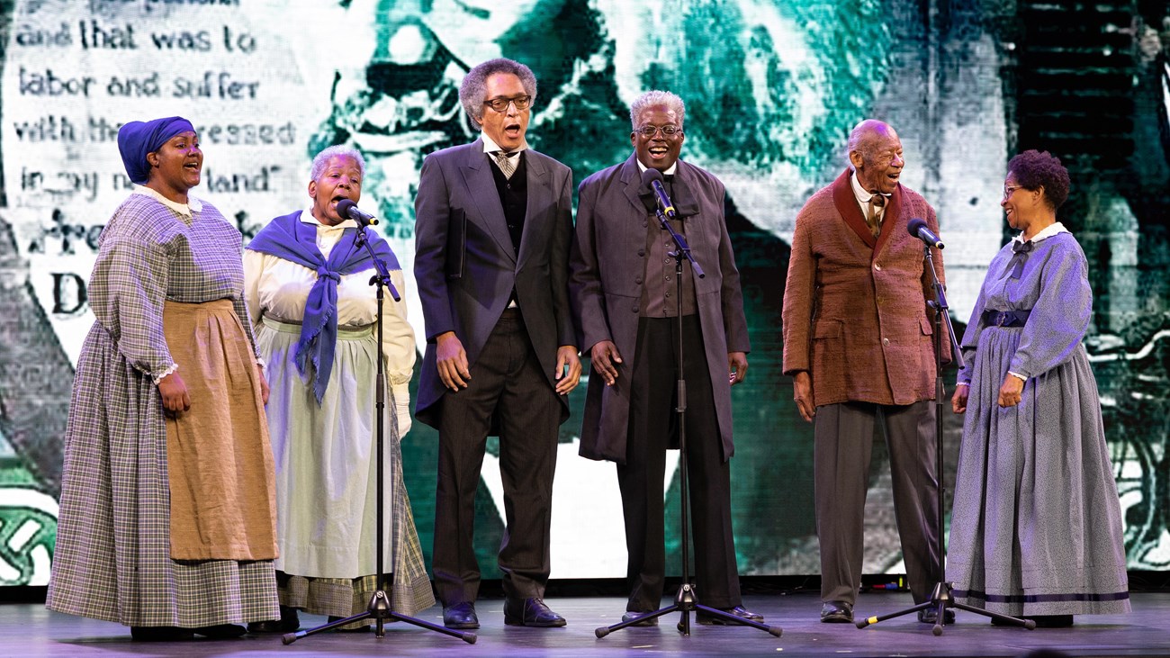 A group of six singers perform on a stage.