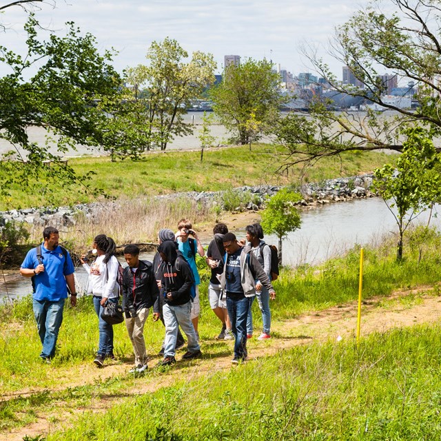 A group of teenagers walks along a path near a wetland.