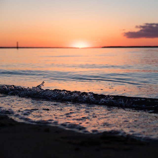 Sun sets over water as seen from a coast line.