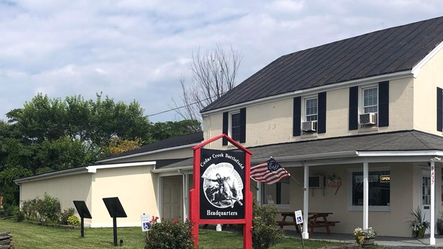 A white farmhouse-like building stands on a rural property with a large sign in front.