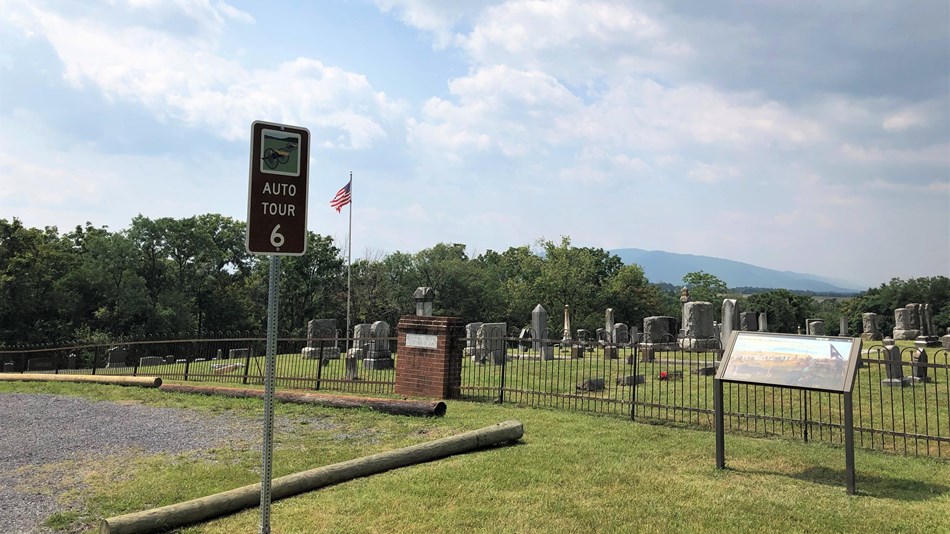 A road sign labeled auto tour 6 marks a tour stop and exhibit by a cemetery.