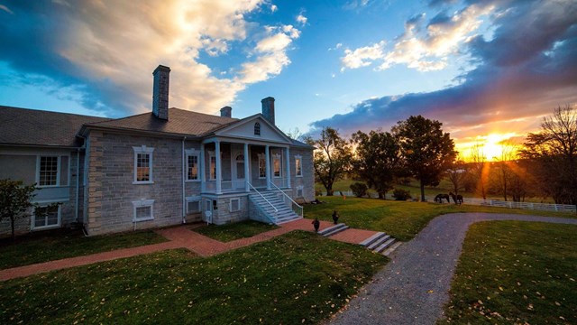The rising sun lights the clouds over an antebellum stone mansion with a white portico.