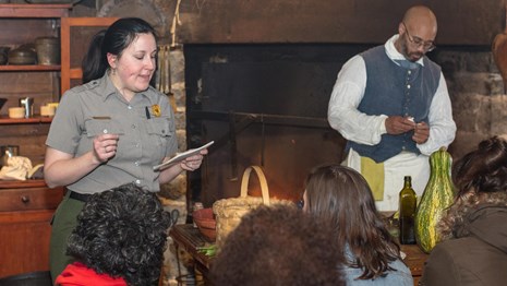 A ranger and a demonstrator demonstrate for an audience in a historic kitchen.