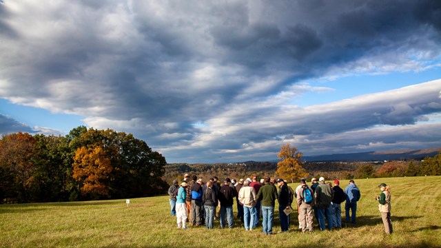A group of twenty people gathers on a lawn during a sunny fall day.