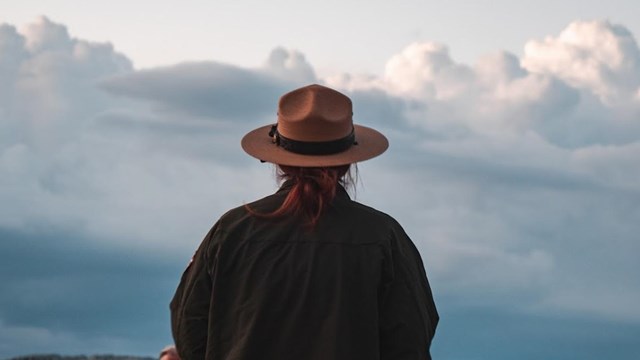 A uniformed ranger stands before a late sunset