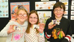 Three kids holding their fourth grade park passes.