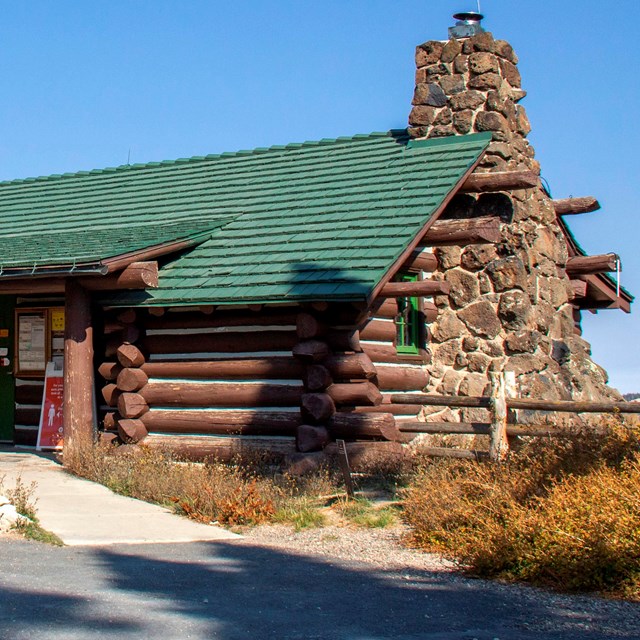 Log and stone one-story building with a green shingle roof.