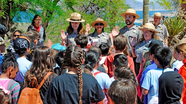 Park rangers raising their hands in front of a group of school children