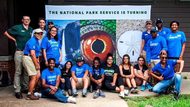 Young adults gathered around in front of a centennial banner.