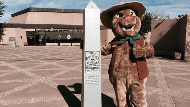 Ground squirrel mascot stands next to boundary monument in front of park cultural center