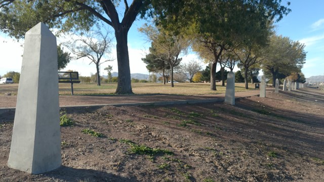 A row of white concrete obelisks line the boundary of the park alongside a road
