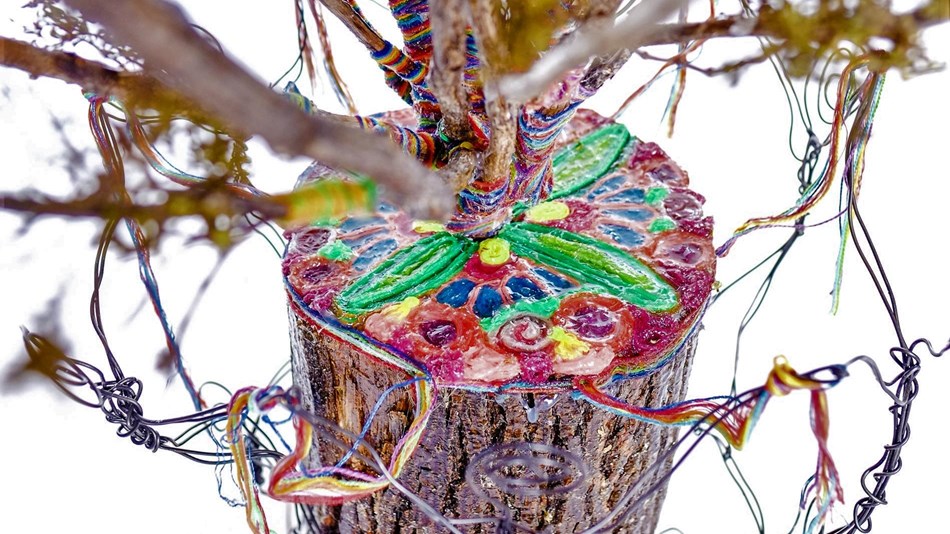 close-up of sculpture showing tree trunk with painted flowers on a cut end with stems and wire