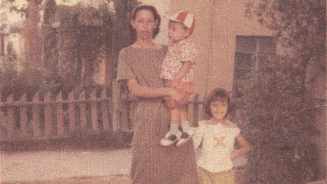 Woman stands with two small children in front of house