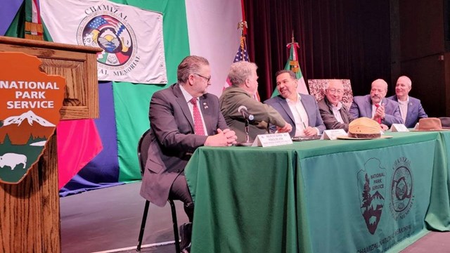 Six people seated at a table signing an agreement