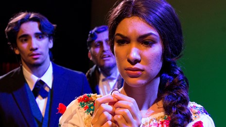 A woman in traditional Mexican attire in the foreground with two men behind her
