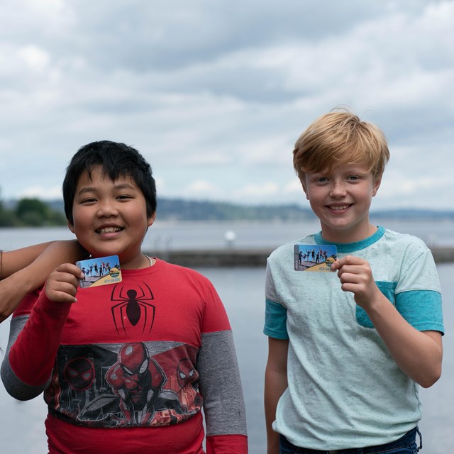 Three smiling kids holding plastic cards in front of body of water