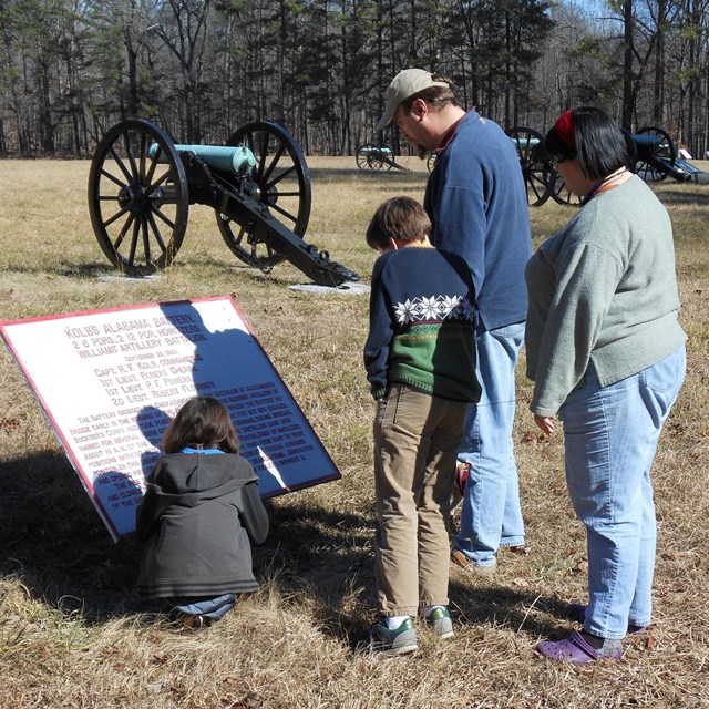 A family looks at a metal tablet on the battlefield