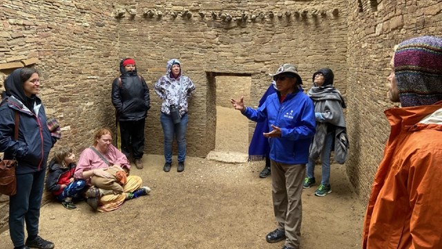 A volunteer talking with a group of visitors inside a room of Pueblo Bonito.